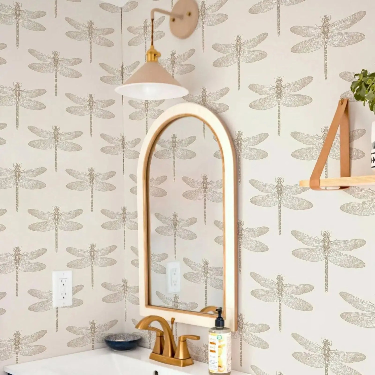 Bathroom with dragonfly patterned wallpaper, arched mirror, and gold fixtures.