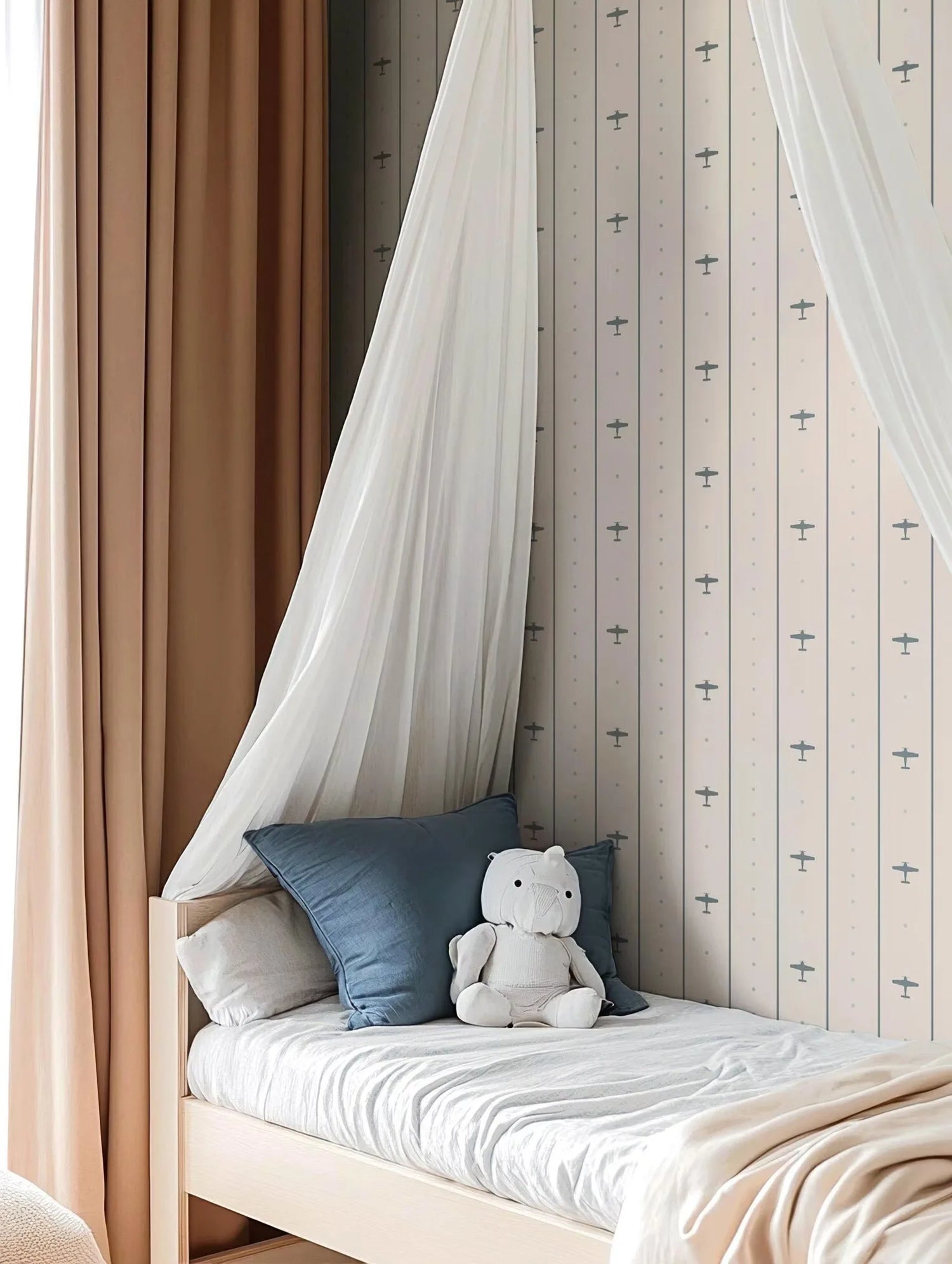 Children's bed with canopy, pillows, and a teddy bear against a patterned wall.