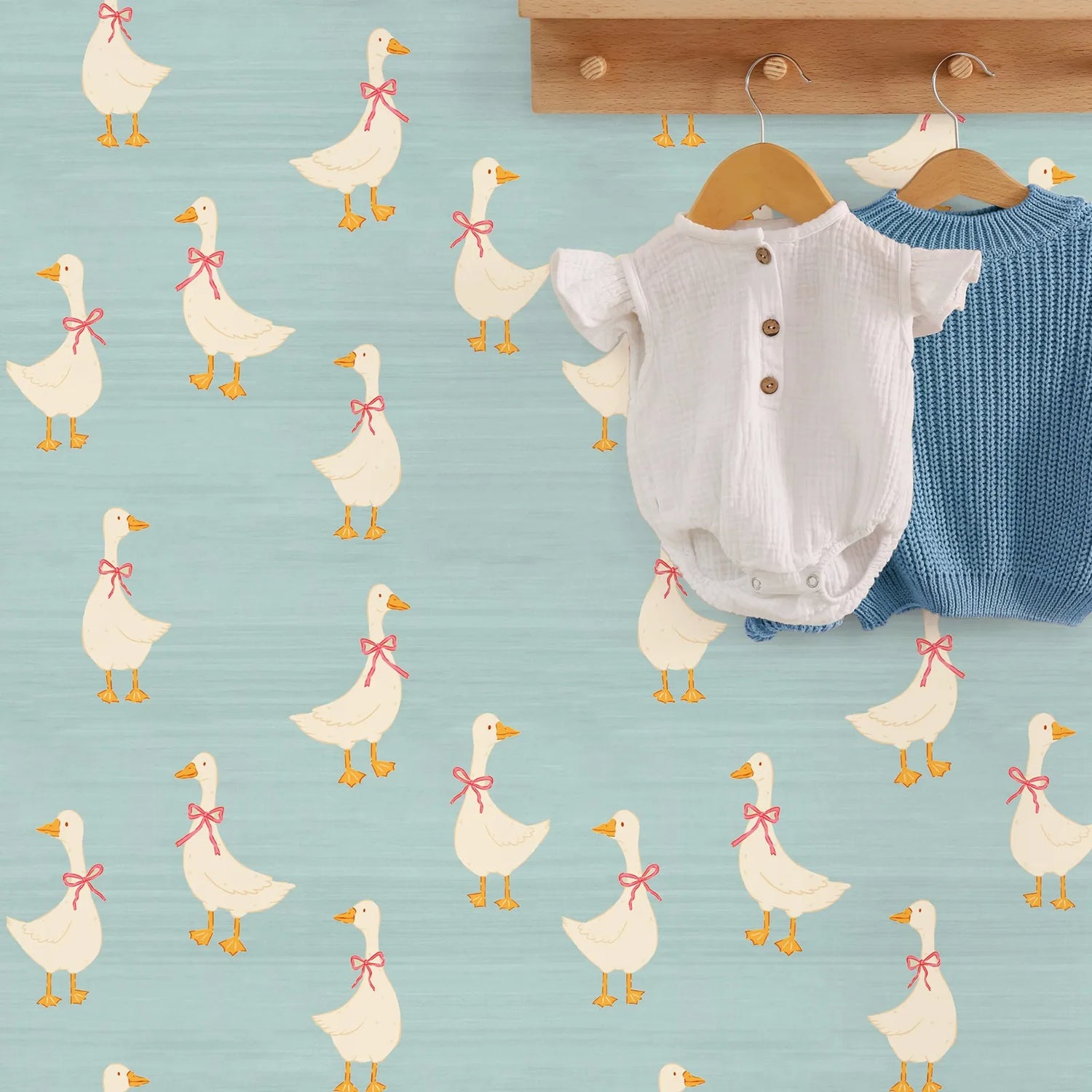 Baby romper and blue knitted item on hangers with duck pattern on light blue background
