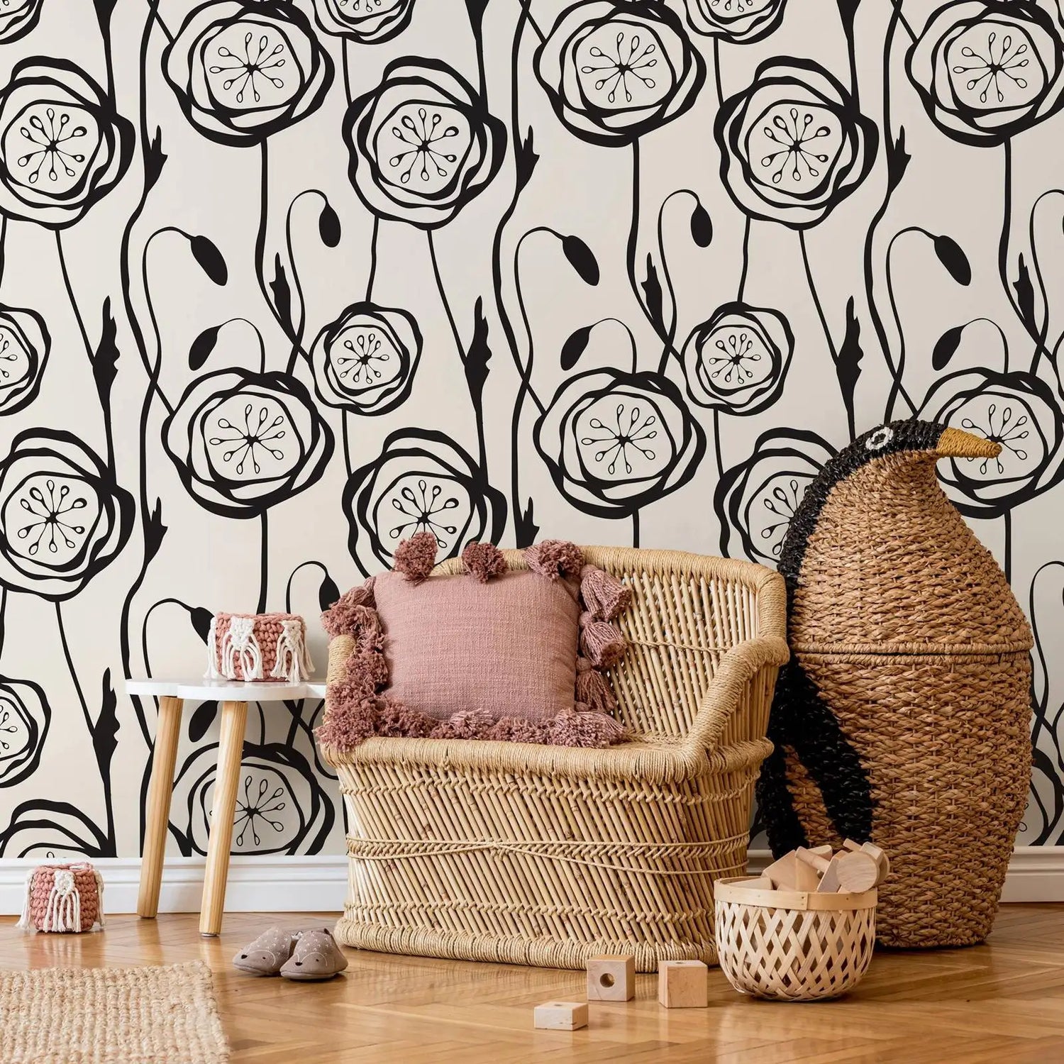 Wicker chair with pink cushion against a black and white floral wallpaper.