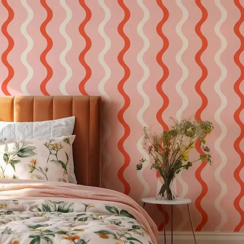 Bedroom with wavy patterned wallpaper, floral bedding, and a vase of flowers on a small table.