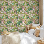 Tropical leaf and flower patterned wallpaper in a bedroom setting with a bed and wicker chair.