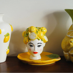 Decorative ceramic piece of a woman's head with lemon design, surrounded by similar items on a wooden surface.