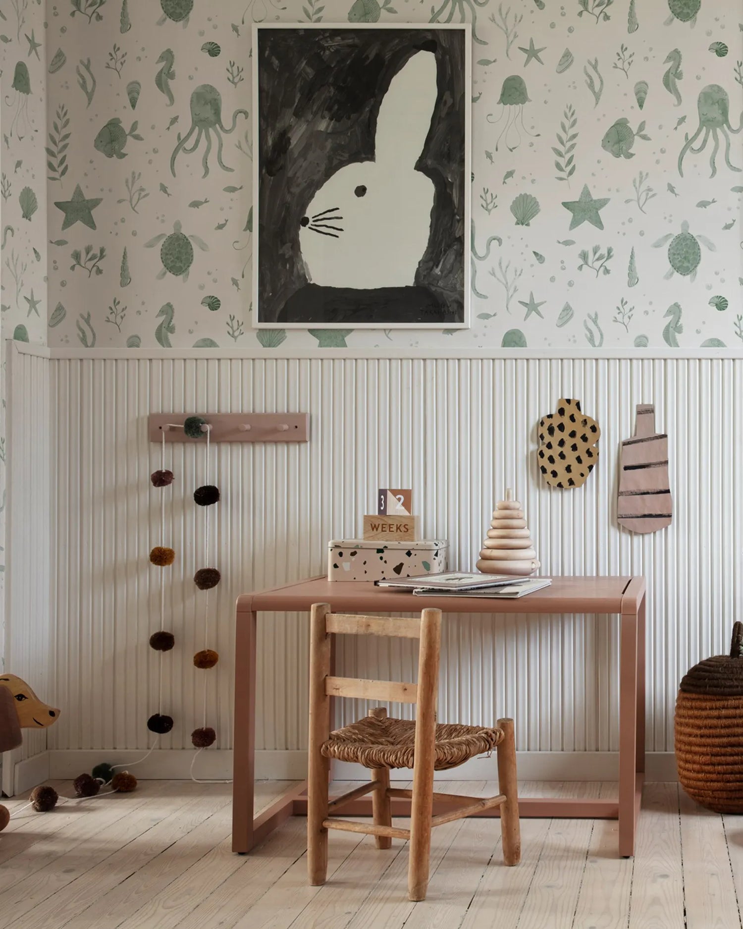 Children's room with wooden table, chair, and decorative elements on a light-colored wall.
