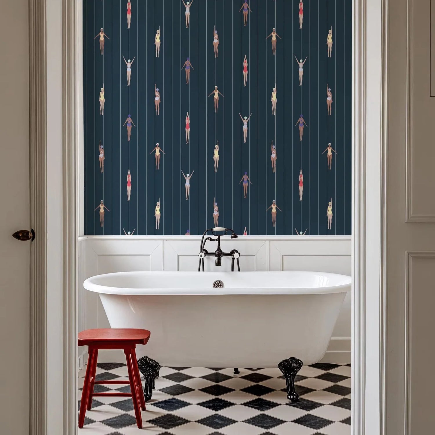 Bathroom with freestanding bathtub, red stool, and patterned wallpaper.