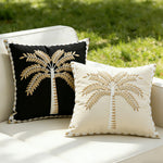 Two decorative pillows with palm tree designs on a white outdoor sofa.