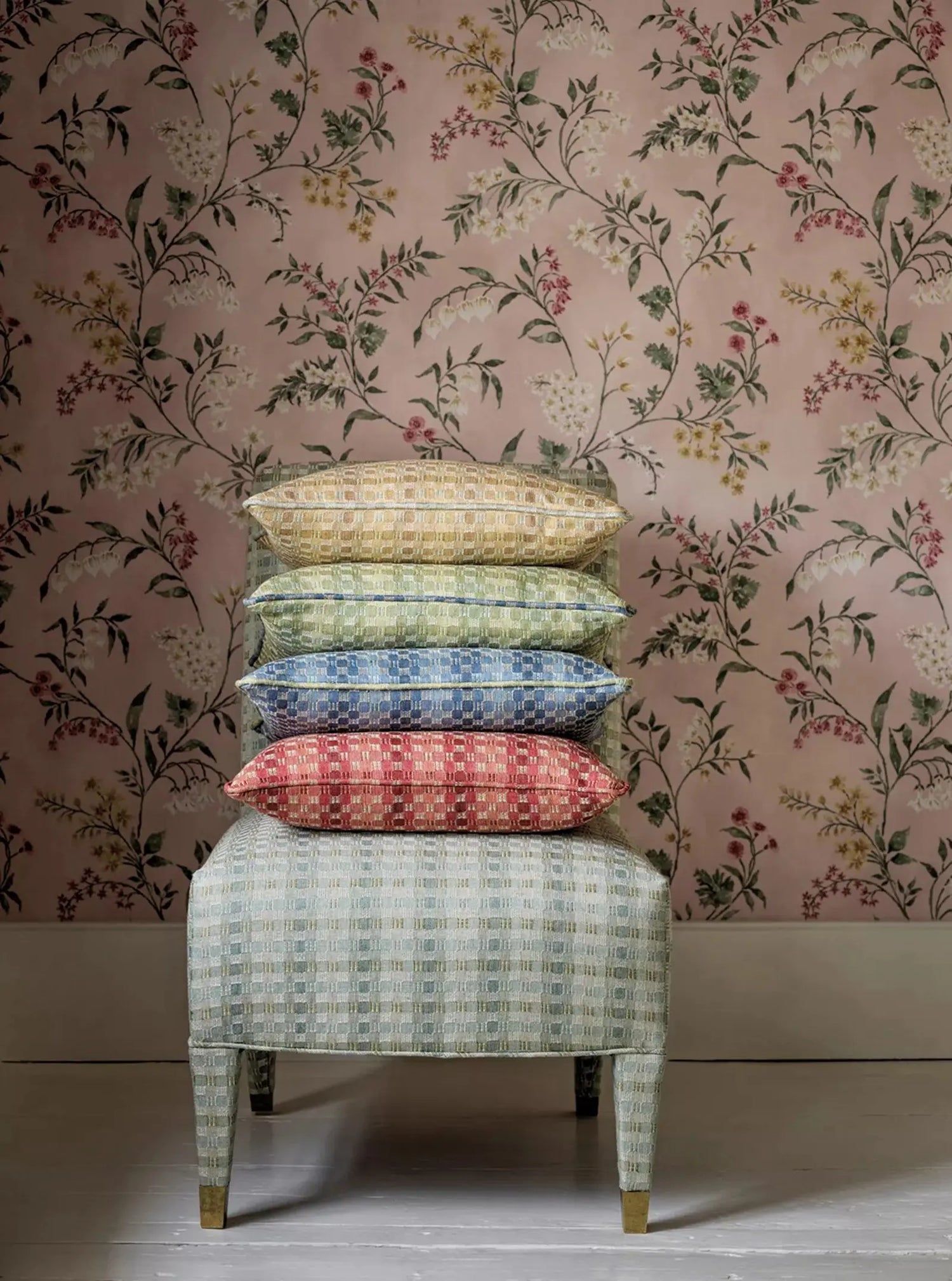 Stack of patterned cushions on a stool against a floral wallpapered wall