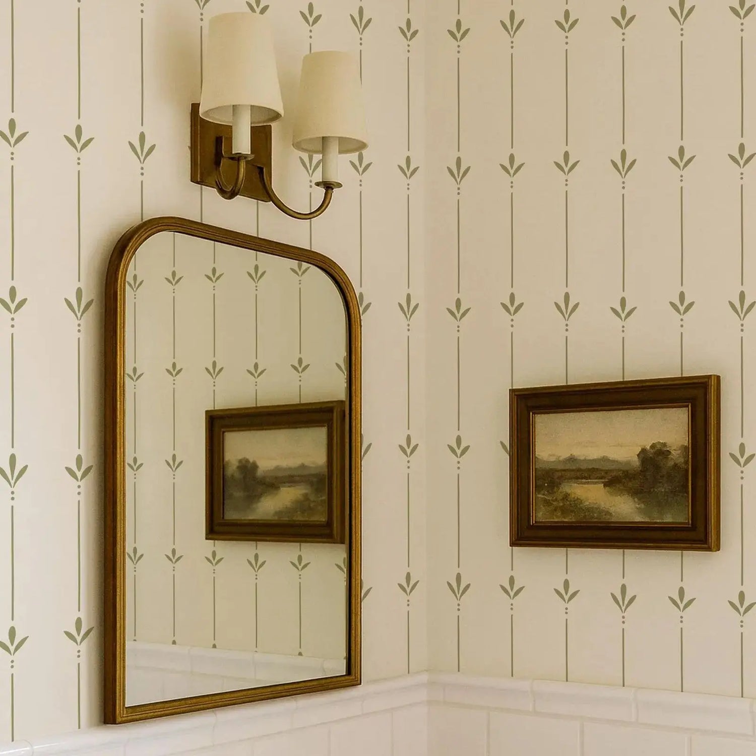Decorative wall with mirror, framed pictures, and wall sconce against a patterned wallpaper.