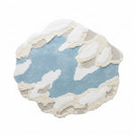 Round cloud-shaped rug on a light wooden floor with a chair and window in the background.