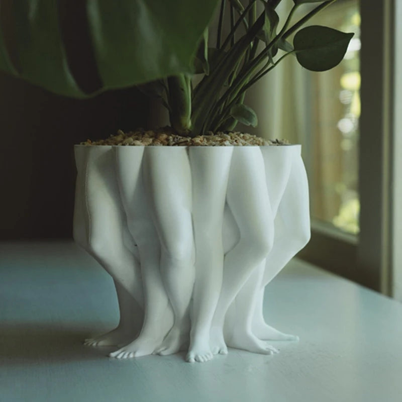 White ceramic planter shaped like legs on a light surface with a blurred background