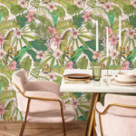 Dining table setting with pink chairs against a tropical leaf and floral wallpaper.