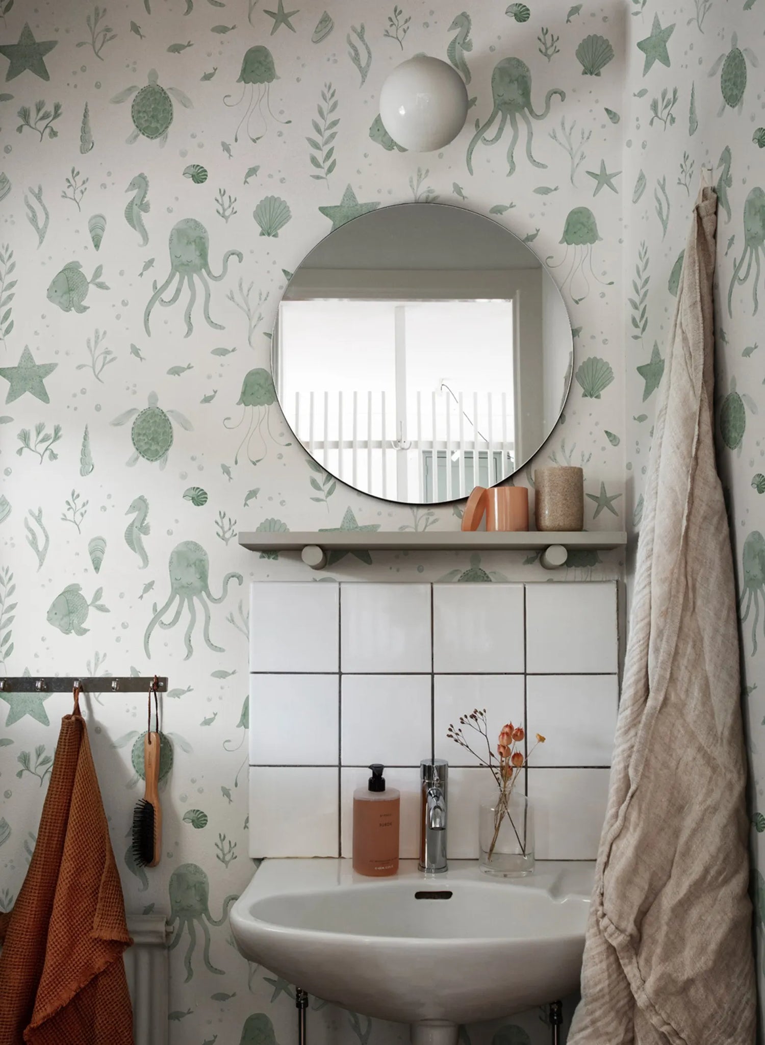Bathroom with green underwater-themed wallpaper, round mirror, and sink.