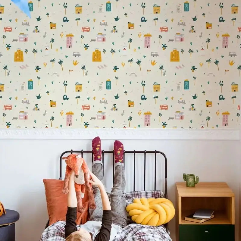 Child playing with a stuffed animal on a bed with colorful wallpaper featuring small illustrations.