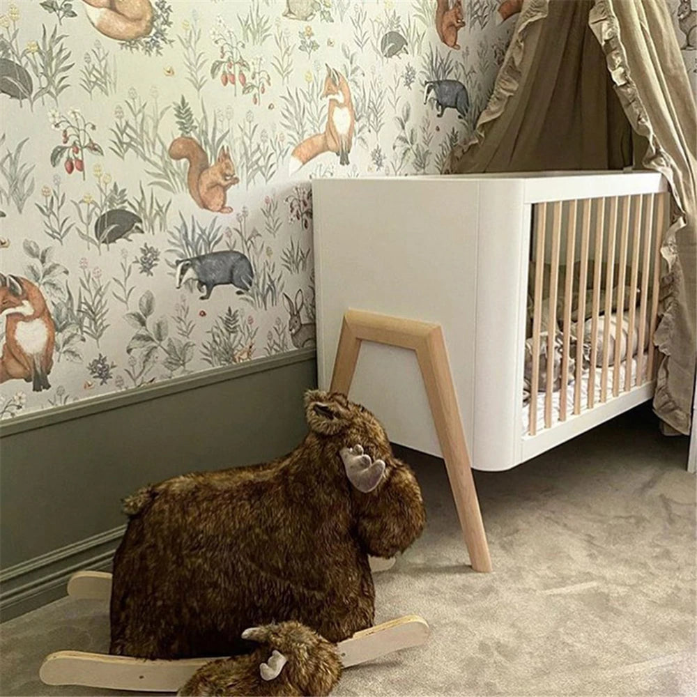 Children's room with a crib, wooden rocking horse, and forest-themed wallpaper.