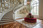 Staircase with decorative wall art, a red cushioned ottoman, and a large rug.