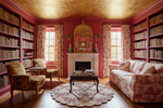 Living room with red walls, bookshelves,  scallop round rug, a fireplace, and patterned furniture.