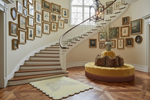 Staircase with decorative scalloped butterfuly rug, wall art and a round ottoman in a well-lit room.
