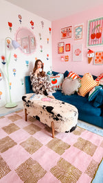 Woman sitting on a colorful couch in a room with floral wall decals and a patterned rug.
