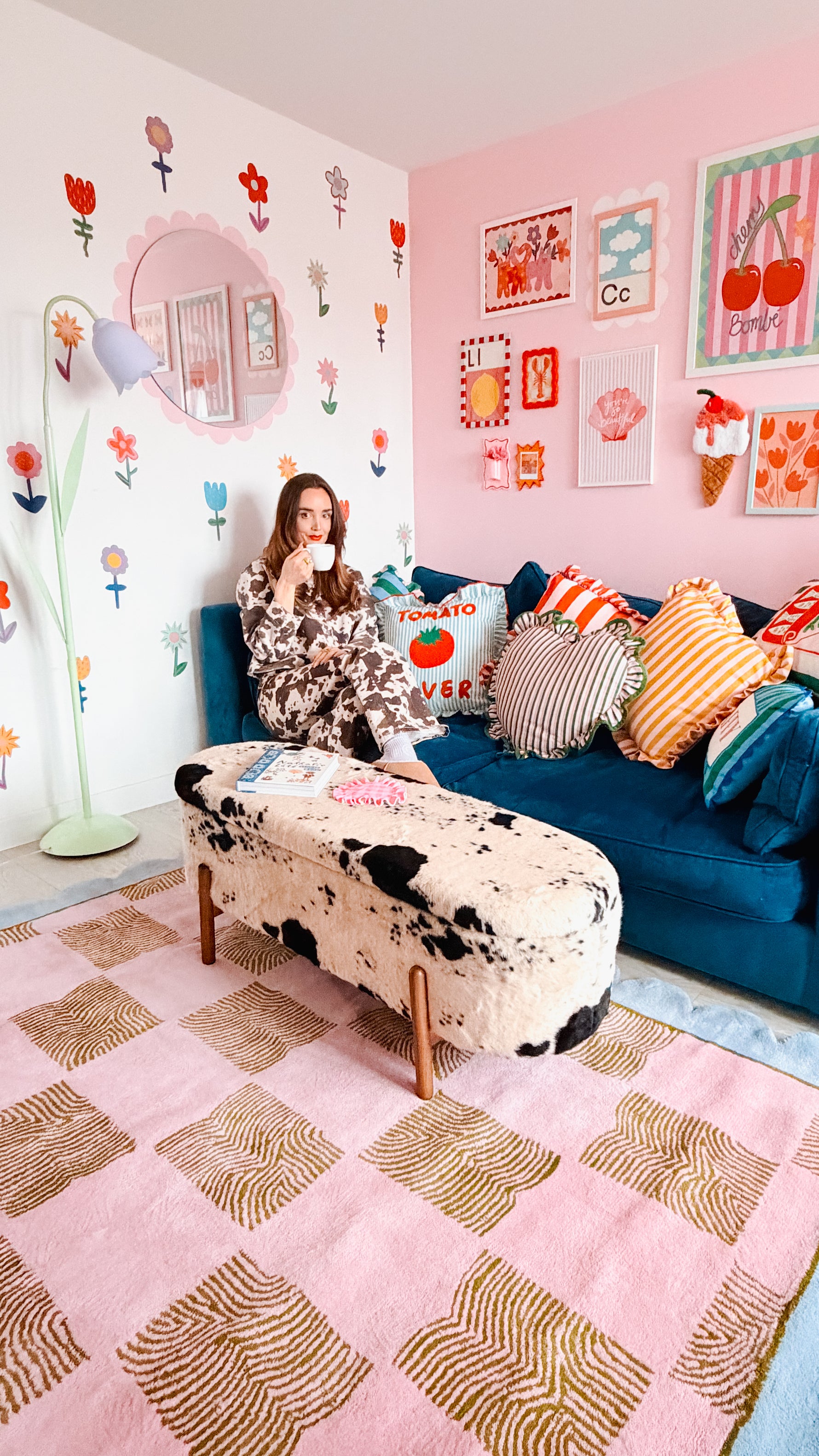 Woman sitting on a colorful couch in a room with floral wall decals and a patterned rug.