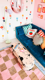 Children's room with a blue bed, colorful rug, and a cow-shaped ottoman on a pink checkered rug.