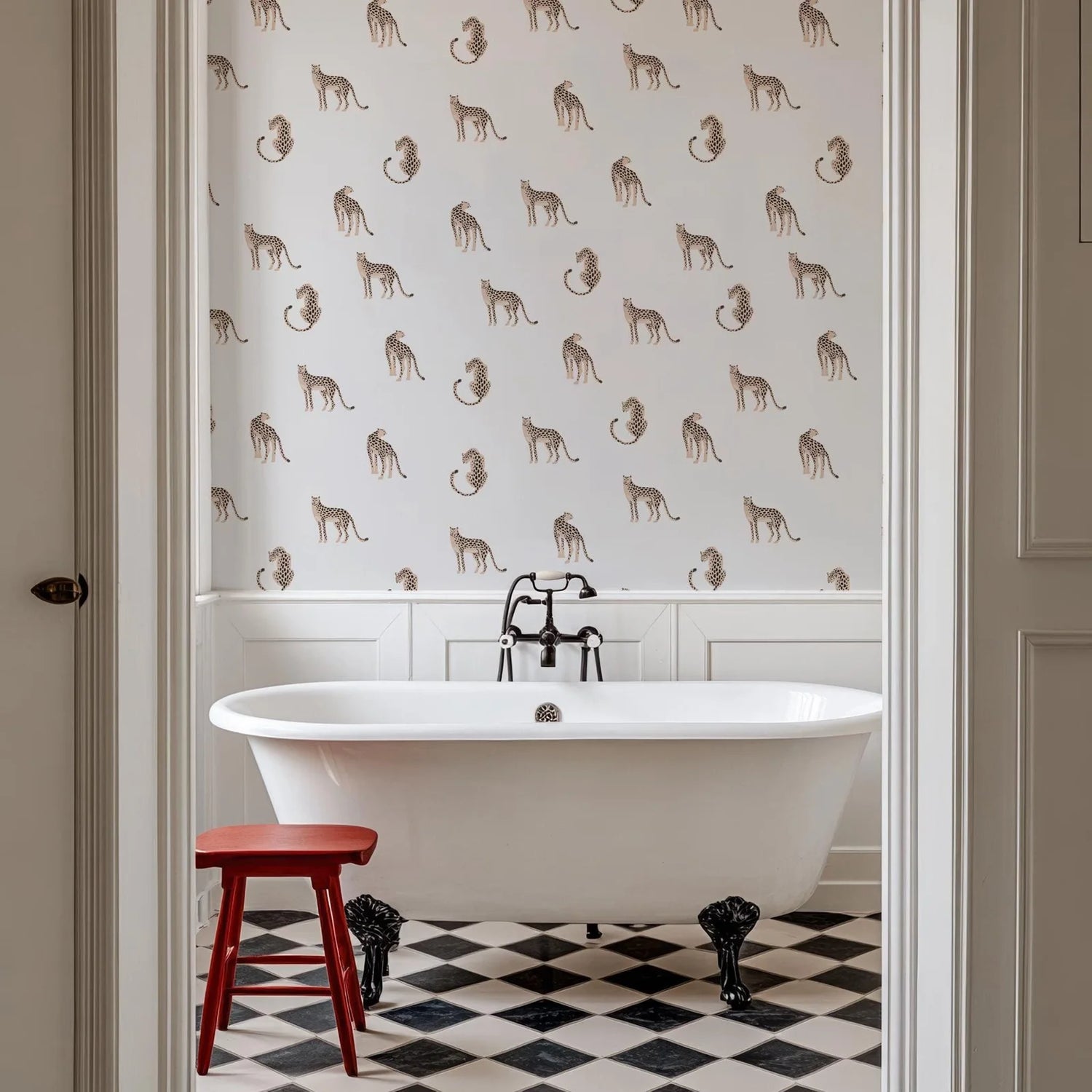 Bathroom with a freestanding bathtub, red stool, and patterned wallpaper.