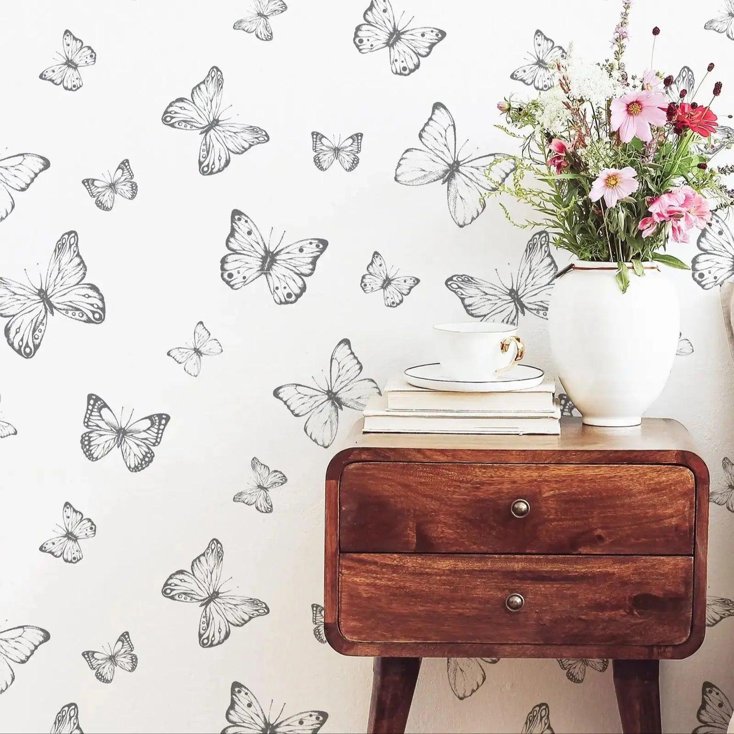 Wooden side table with a vase of flowers against a wall with butterfly wallpaper