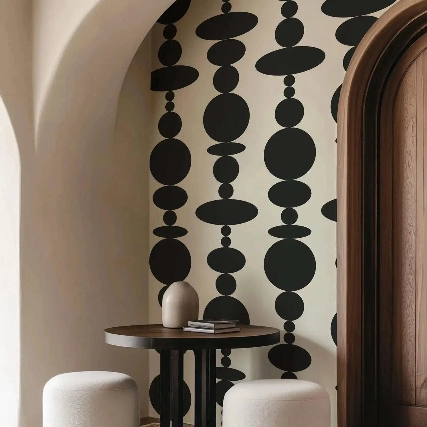 Decorative wall with black circular pattern, table with vase and books, and white stools.