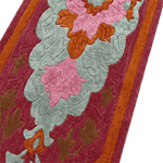 Close-up of a textured fabric with floral patterns in pink, orange, and gray on a red background.