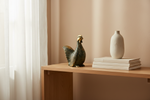 Solid brass chicken figurine displayed on a console table with ceramic vases and stacked books