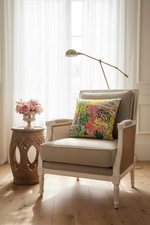 An olive green velvet loveseat sofa with a colorful tropical print accent pillow, styled in a room setting with a side table and vase.