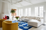 Modern living room with a white sectional sofa, yellow chairs, and a blue rug.