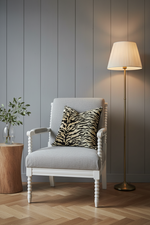 A white slipcovered sofa with a textured black and beige zebra-print throw pillow, set against a warm beige wall and light wood floor.