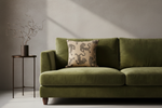 An olive green velvet sofa in a modern living room setting, styled with a beige throw pillow featuring a dark gray leopard print, next to a small dark metal side table with a decorative dried branch vase.