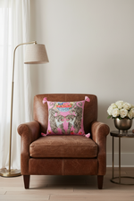 A pink decorative throw pillow with a tiger print and colorful floral details, styled on a white slipcovered sofa in a living room setting.