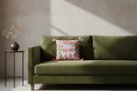 A pink decorative throw pillow with a tiger print and colorful floral details, styled on a white slipcovered sofa in a living room setting.