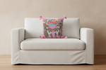 A pink decorative throw pillow with a tiger print and colorful floral details, styled on a white slipcovered sofa in a living room setting.