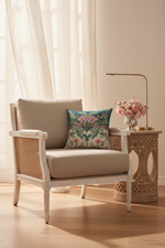 A brown leather wingback armchair in a styled room corner, featuring a colorful floral patterned throw pillow. A gold floor lamp stands to the left, and a small side table with white flowers is on the right.