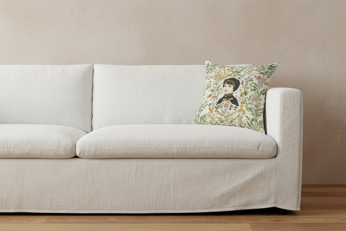 A white fabric slipcovered sofa with a decorative throw pillow featuring a vintage-style illustration of a woman in a kimono surrounded by floral patterns, set against a textured beige wall and light wood floor.