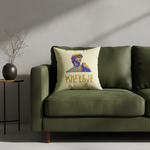 A cream throw pillow with a colorful graphic of a woman's profile and the text 'WHERE LOVE' in gold, styled on a beige armchair in a bright, modern living room setting.