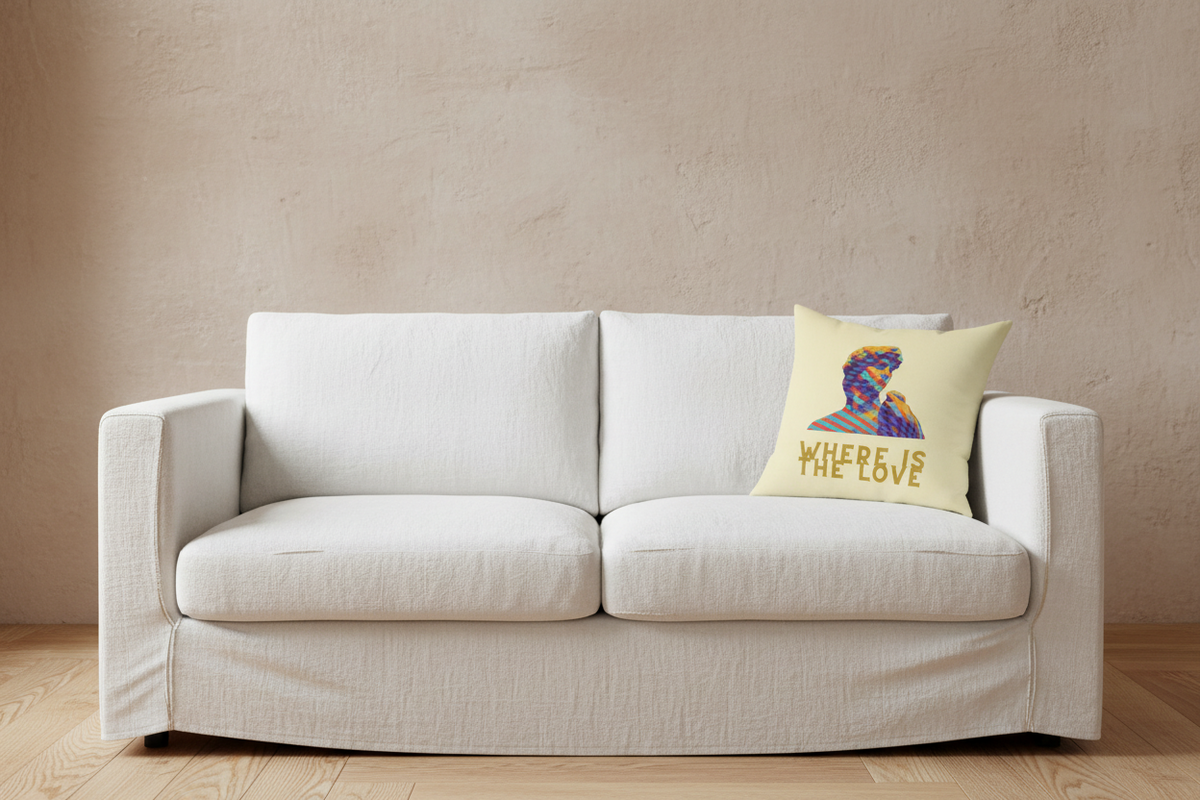 A cream throw pillow with a colorful graphic of a woman's profile and the text 'WHERE LOVE' in gold, styled on a beige armchair in a bright, modern living room setting.