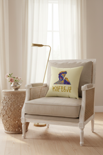 A cream throw pillow with a colorful graphic of a woman's profile and the text 'WHERE LOVE' in gold, styled on a beige armchair in a bright, modern living room setting.