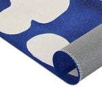 Abstract Blue and White Geometric Rug corner curl close-up showing cobalt blue surface texture and grey backing material and serged edge