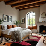 abstract odyssey hand tufted viscose rug in a rustic bedroom with wood-beam ceiling, arched window, lit fireplace and terracotta pillows