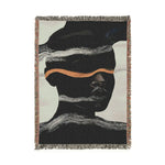 Fringed woven throw blanket with dark silhouetted abstract face, horizontal white wave bands and copper stripe, off-white ground, portrait