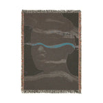 Reverse side of woven blanket with dark brown cotton ground, teal horizontal stripe and abstract face in subtle tones, fringe edges