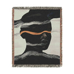 Square-cropped woven throw blanket with dark abstract face silhouette, white wave bands and copper-gold horizontal stripe, fringe edges