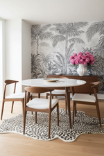 Dining room with a round table, chairs, cheetah print rug, and a floral arrangement against a tropical wallpaper.