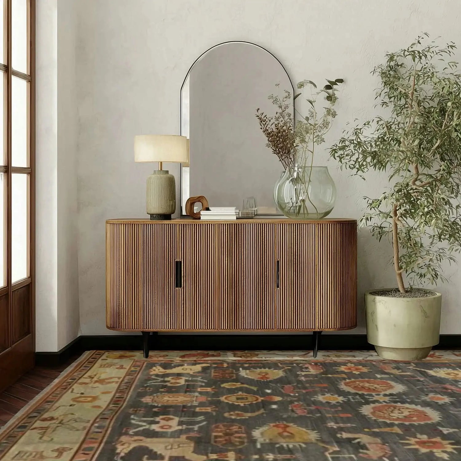 Wooden sideboard with decorative items and persian dark gary rug in a room with a large mirror and plant.