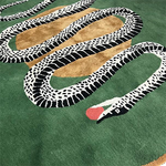 Angled view of round snake rug, monochrome serpent and red apple on green hand tufted wool