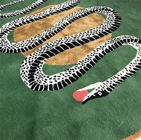 Angled view of round snake rug, monochrome serpent and red apple on green hand tufted wool